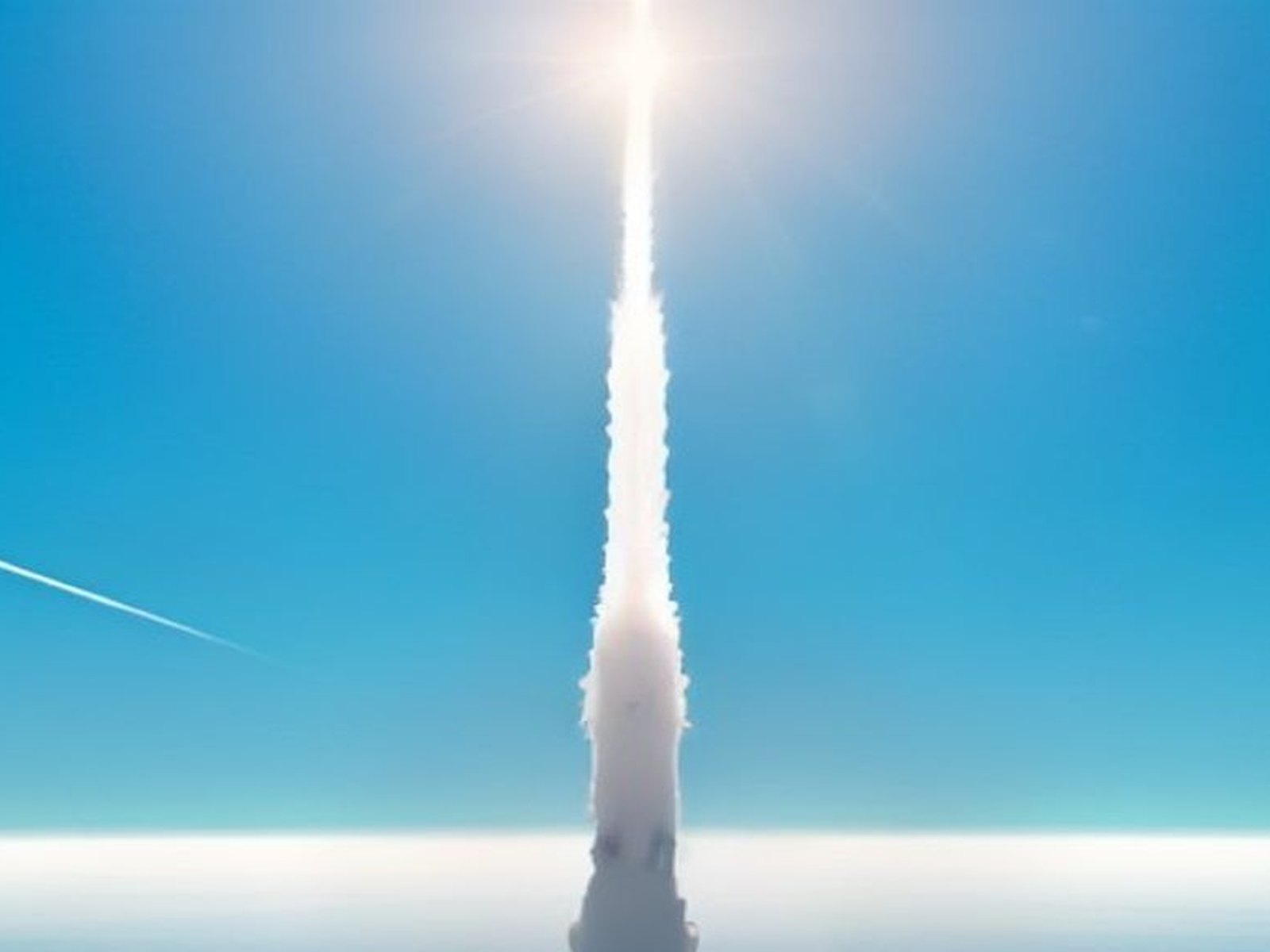 A rocket launch trail against a blue sky